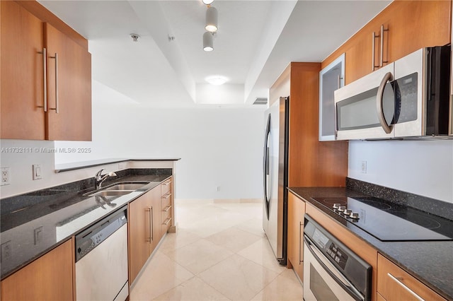 kitchen featuring sink, light tile patterned floors, dark stone countertops, a raised ceiling, and stainless steel appliances