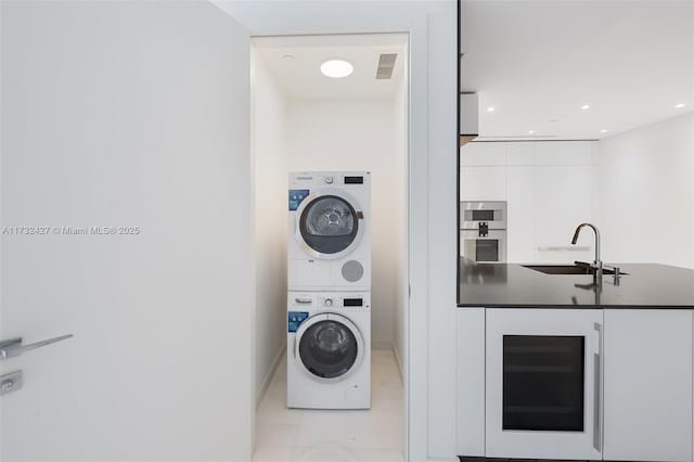 clothes washing area featuring stacked washer and dryer, recessed lighting, visible vents, a sink, and beverage cooler