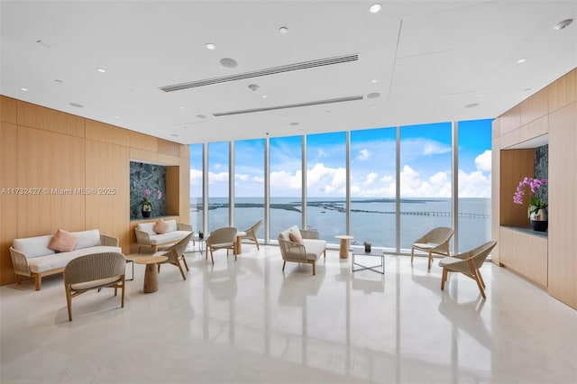 interior space featuring a water view, wood walls, plenty of natural light, and a wall of windows