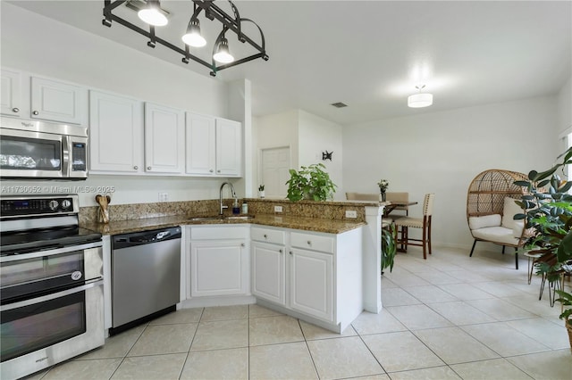 kitchen featuring sink, white cabinetry, appliances with stainless steel finishes, kitchen peninsula, and dark stone counters