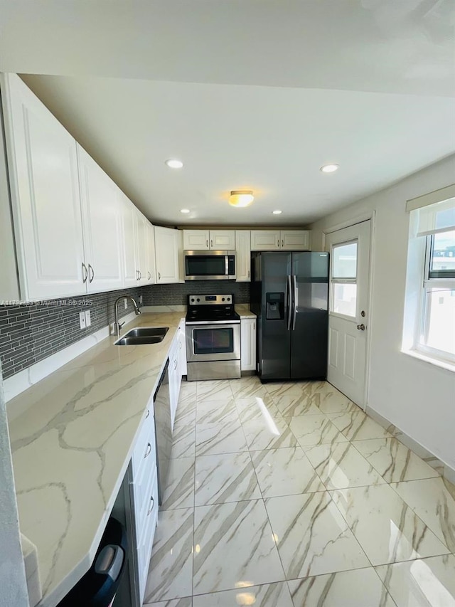 kitchen with sink, light stone counters, stainless steel appliances, decorative backsplash, and white cabinets