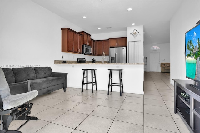 kitchen with a breakfast bar area, light tile patterned floors, kitchen peninsula, stainless steel appliances, and light stone countertops