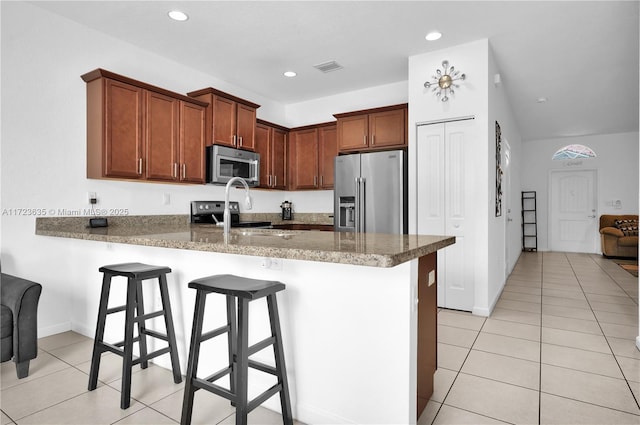 kitchen featuring sink, appliances with stainless steel finishes, dark stone countertops, a kitchen bar, and kitchen peninsula