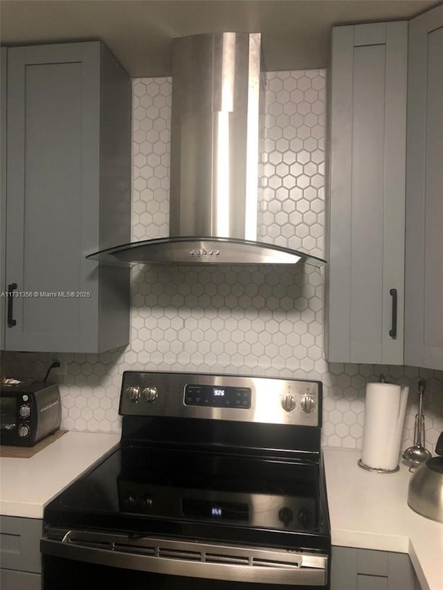 kitchen featuring tasteful backsplash, electric range, gray cabinets, and wall chimney exhaust hood