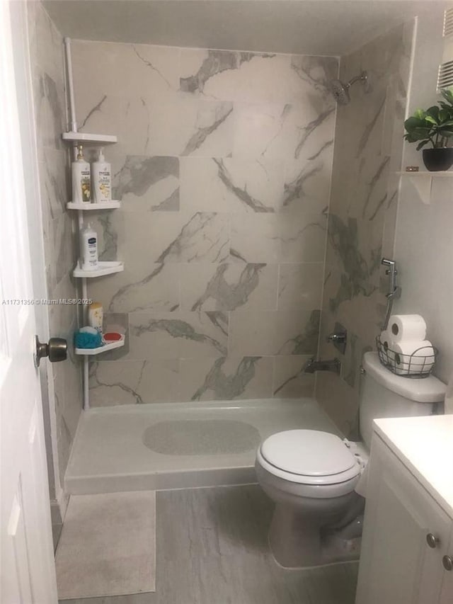 bathroom featuring vanity, toilet, and a tile shower