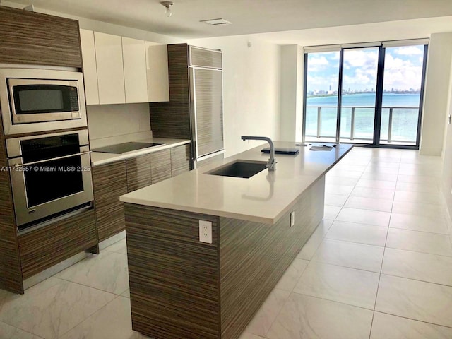 kitchen featuring appliances with stainless steel finishes, sink, white cabinets, a kitchen island with sink, and a water view