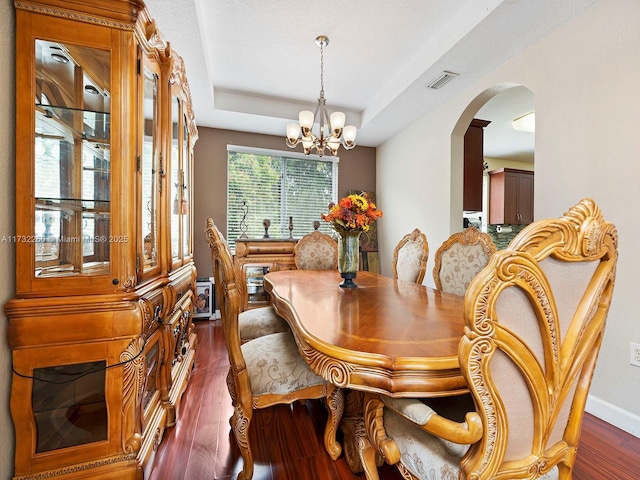 dining room with a chandelier, dark hardwood / wood-style flooring, and a raised ceiling