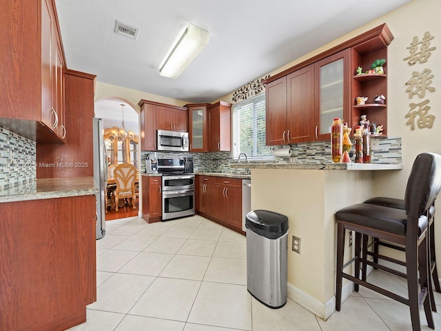 kitchen featuring an inviting chandelier, backsplash, light tile patterned floors, and appliances with stainless steel finishes