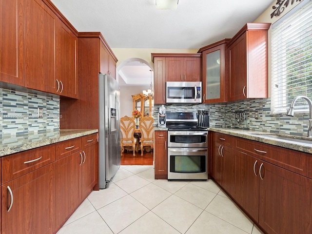 kitchen with sink, tasteful backsplash, light stone counters, light tile patterned floors, and stainless steel appliances