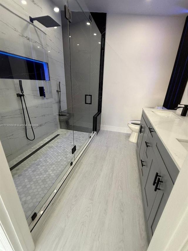 bathroom featuring wood-type flooring, toilet, a shower with shower door, and vanity