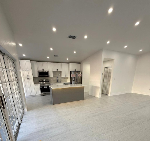 kitchen featuring sink, appliances with stainless steel finishes, white cabinetry, a center island, and light wood-type flooring