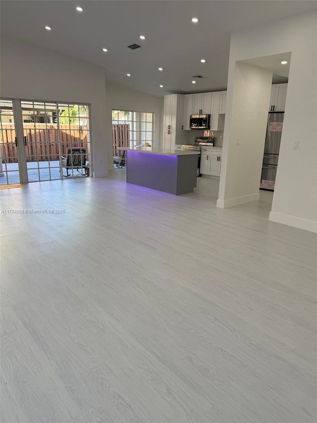 unfurnished living room with lofted ceiling and light wood-type flooring