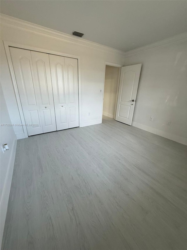 unfurnished bedroom with crown molding, light hardwood / wood-style floors, and a closet