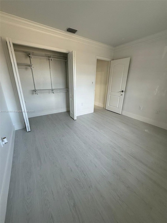 unfurnished bedroom featuring crown molding, hardwood / wood-style floors, and a closet