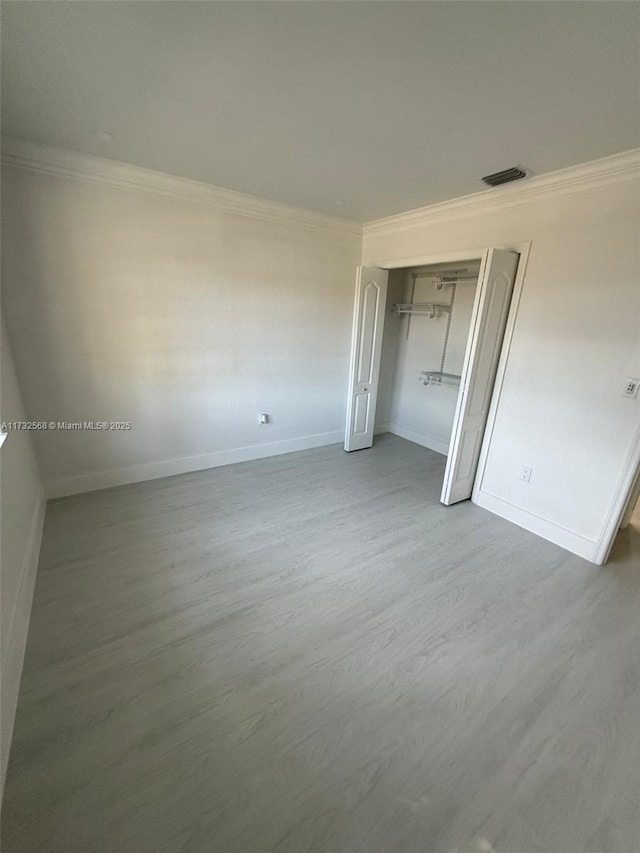 unfurnished bedroom with hardwood / wood-style flooring, ornamental molding, and a closet