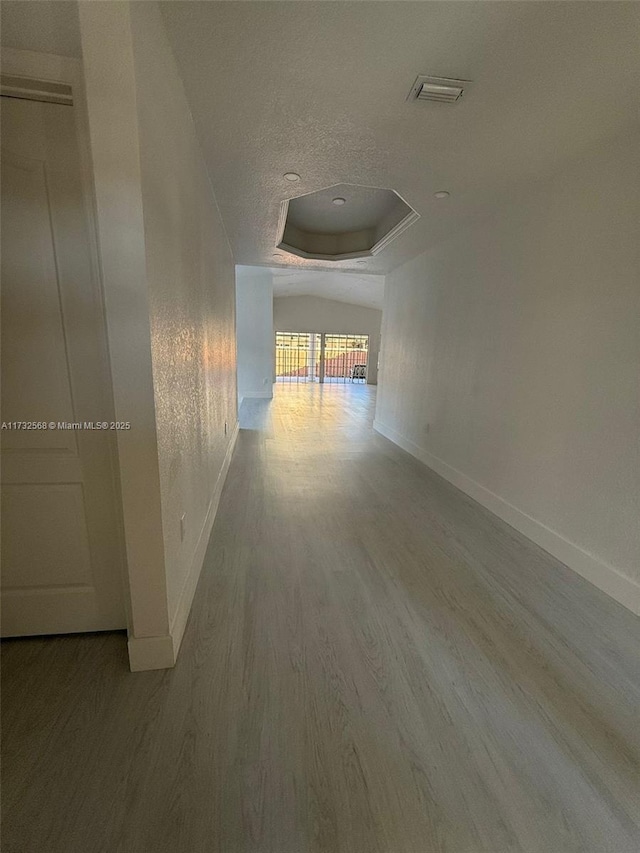 hallway with a tray ceiling, a textured ceiling, and hardwood / wood-style flooring