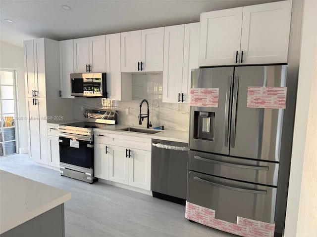 kitchen with sink, stainless steel appliances, white cabinets, and light wood-type flooring