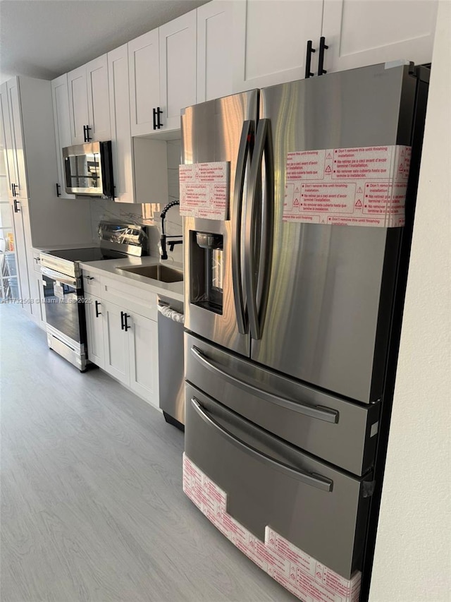 kitchen featuring white cabinetry, sink, stainless steel appliances, and light hardwood / wood-style floors