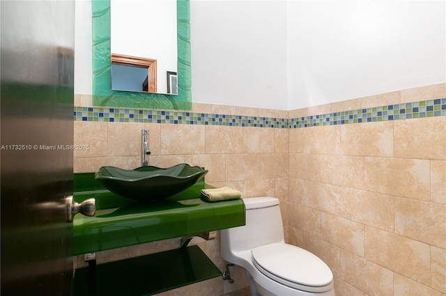 bathroom featuring toilet, tile walls, and a sink