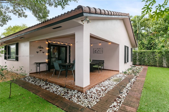 rear view of property with a yard, a patio area, a tiled roof, and stucco siding