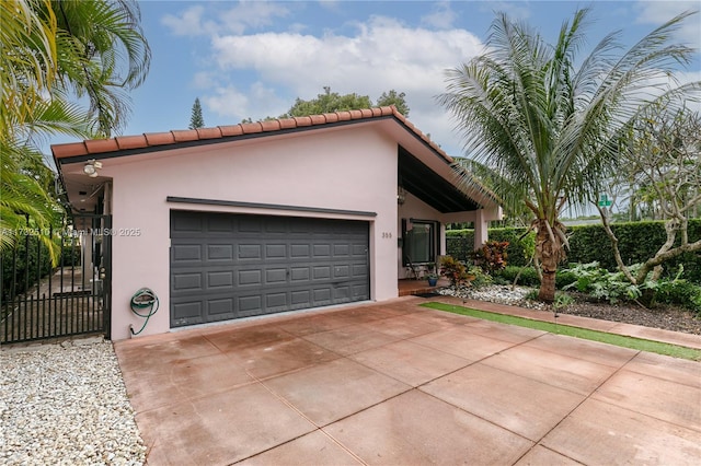 view of front of property with an attached garage, concrete driveway, a tiled roof, a gate, and stucco siding