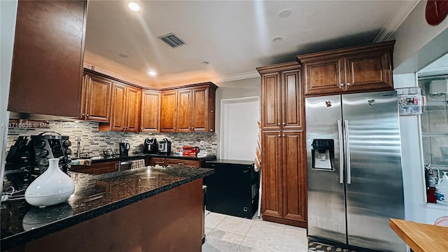 kitchen with crown molding, stainless steel fridge, light tile patterned flooring, decorative backsplash, and dark stone counters