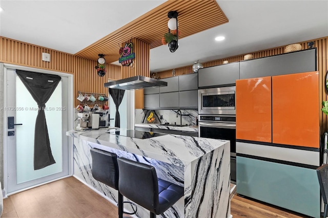 kitchen with light stone countertops, appliances with stainless steel finishes, light wood-type flooring, and extractor fan