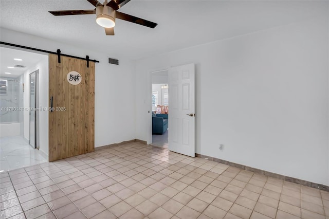 unfurnished room with a barn door, visible vents, ceiling fan, and baseboards