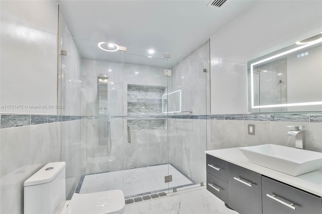 bathroom featuring tile walls, vanity, a shower with shower door, and toilet