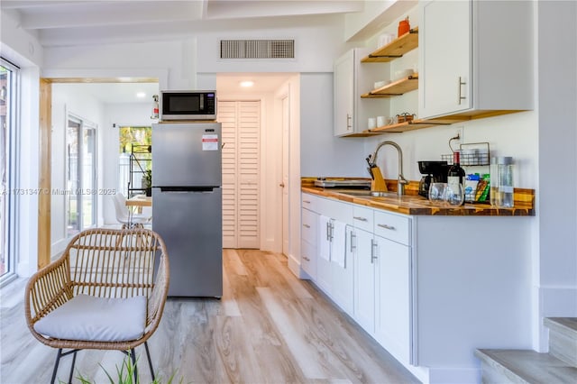 kitchen featuring sink, butcher block countertops, light hardwood / wood-style flooring, stainless steel fridge, and white cabinets