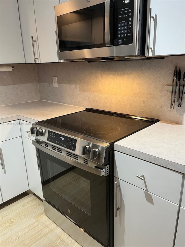 kitchen featuring appliances with stainless steel finishes, light wood-type flooring, decorative backsplash, and white cabinets