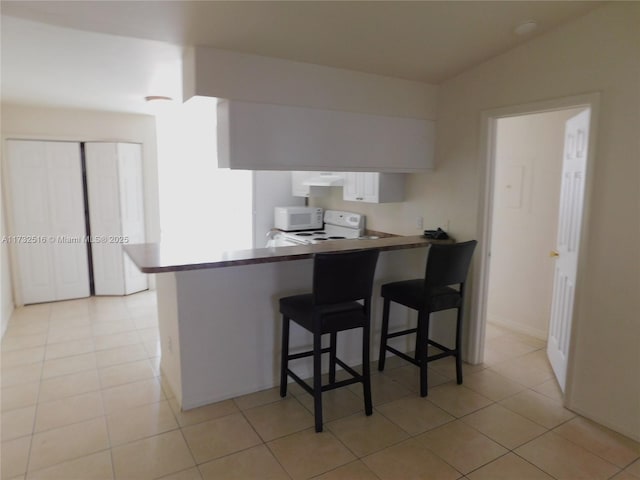 kitchen with a breakfast bar, white cabinetry, light tile patterned floors, kitchen peninsula, and white appliances