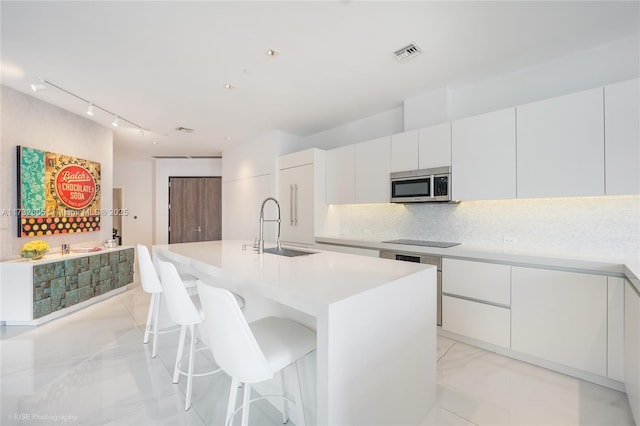 kitchen with a breakfast bar, sink, white cabinetry, a kitchen island with sink, and decorative backsplash