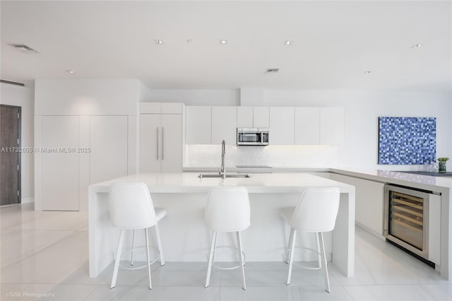 kitchen with sink, tasteful backsplash, a center island, beverage cooler, and white cabinets