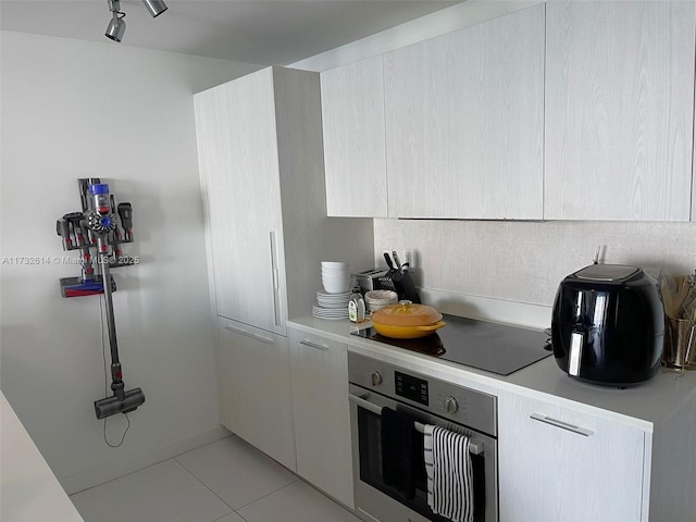 kitchen featuring black electric cooktop, stainless steel oven, and light tile patterned flooring