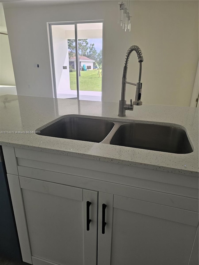 details featuring white cabinetry, light stone countertops, and sink