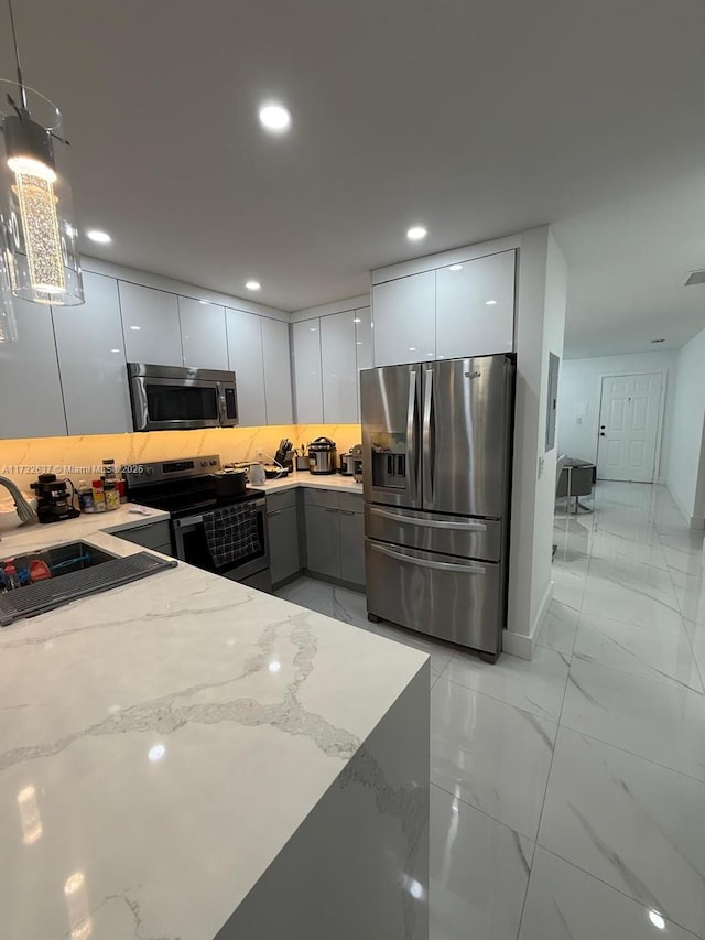 kitchen with appliances with stainless steel finishes, decorative light fixtures, white cabinetry, sink, and light stone counters