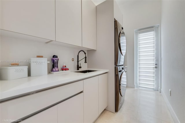 laundry area with cabinets, stacked washer / drying machine, and sink