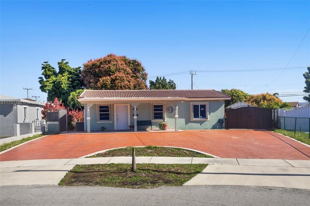 single story home with a tiled roof, a gate, fence, a porch, and stucco siding