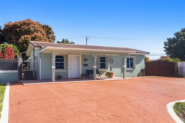 view of front of house with cooling unit, covered porch, a tile roof, a gate, and stucco siding