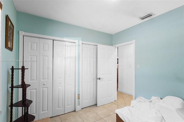 bedroom featuring a textured ceiling, light tile patterned flooring, visible vents, and multiple closets