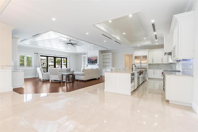 kitchen featuring white cabinetry, a tray ceiling, light stone counters, and a large island with sink