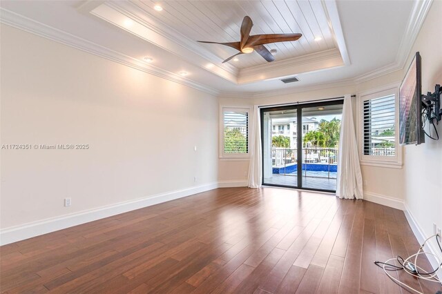 empty room featuring a raised ceiling, crown molding, dark hardwood / wood-style floors, and a wealth of natural light