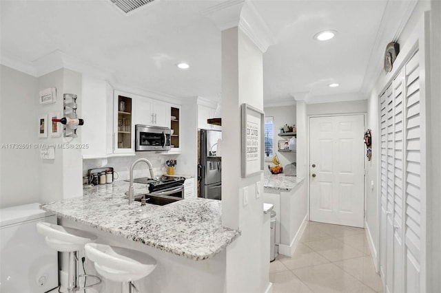 kitchen featuring appliances with stainless steel finishes, a breakfast bar area, white cabinets, light stone counters, and kitchen peninsula