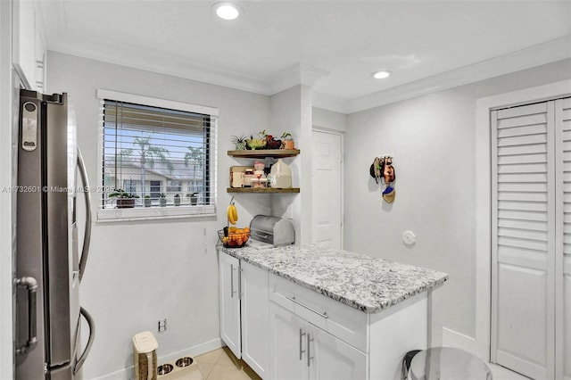 kitchen with light tile patterned flooring, white cabinets, stainless steel fridge, crown molding, and light stone countertops