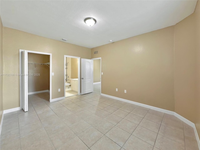 unfurnished bedroom with ensuite bathroom, a walk in closet, a textured ceiling, light tile patterned floors, and a closet