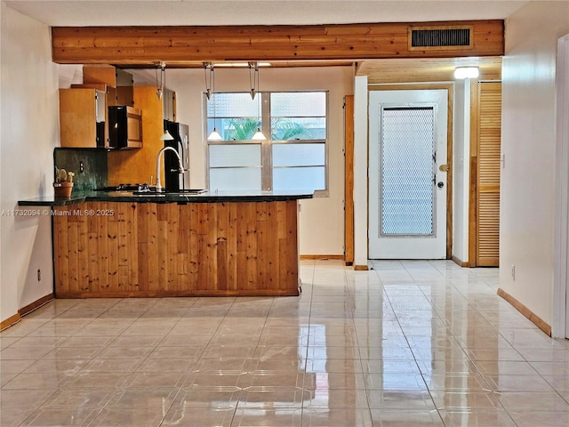 kitchen with tasteful backsplash, visible vents, dark countertops, freestanding refrigerator, and a peninsula