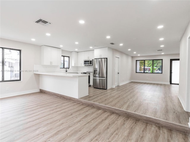 kitchen with sink, white cabinets, kitchen peninsula, stainless steel appliances, and light wood-type flooring