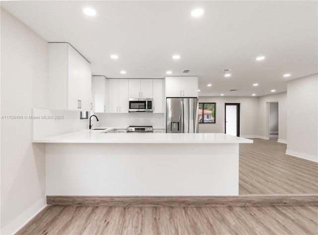 kitchen featuring sink, appliances with stainless steel finishes, kitchen peninsula, light hardwood / wood-style floors, and white cabinets