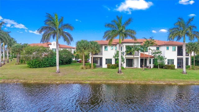 back of property featuring a balcony, a water view, and a lawn